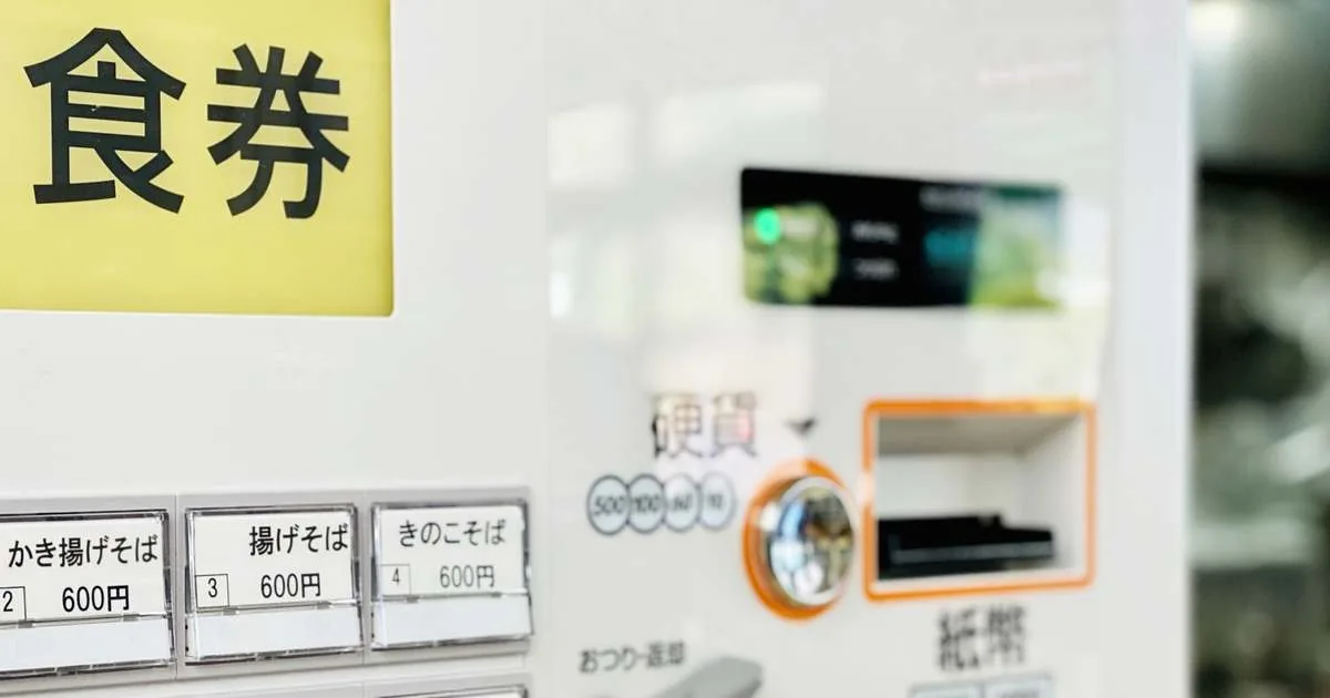 A Japanese meal ticket vending machine with a food ticket sign, coin slot and buttons showing dish names and prices